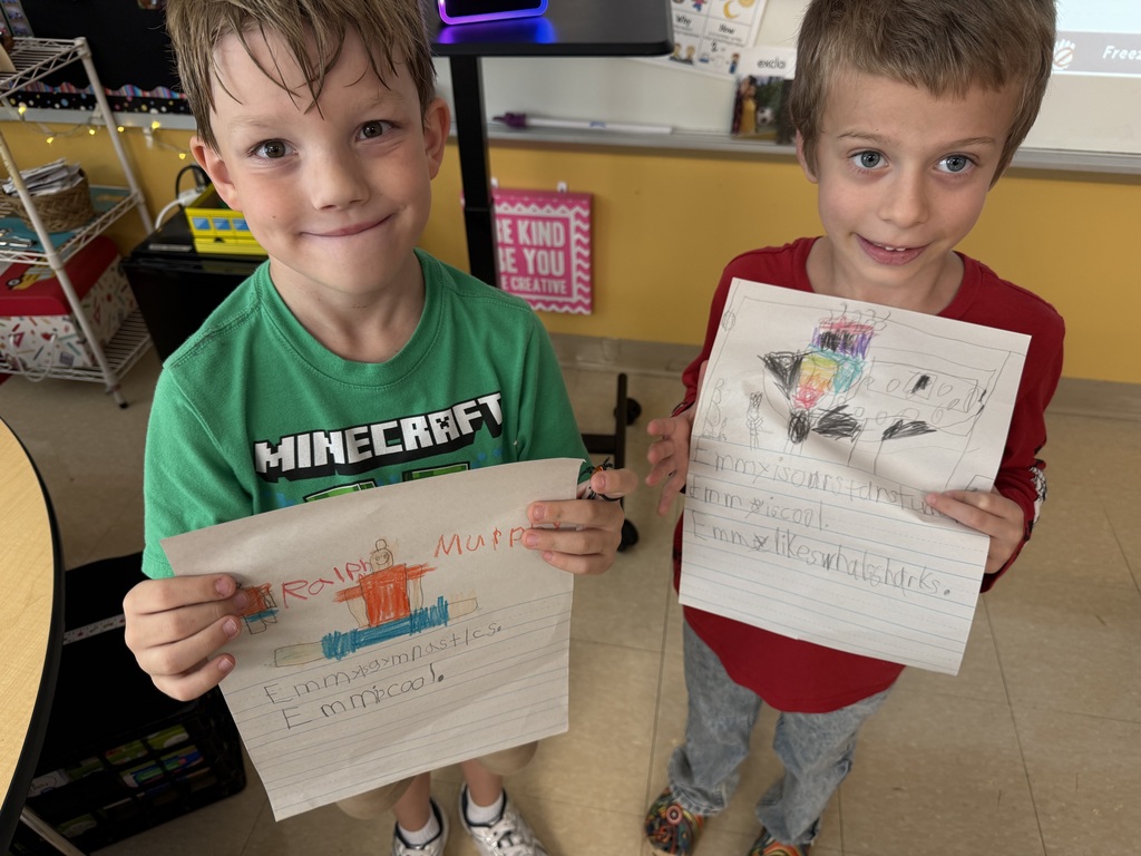 Two boys hold up their homework. One wears a Minecraft t-shirt and the other a red shirt.