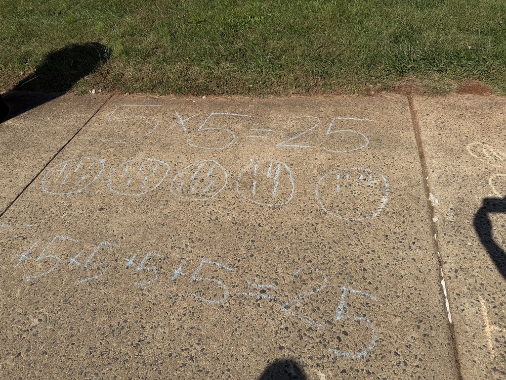 Chalk numbers on a concrete sidewalk, with a shadow of a person nearby, and a patch of green grass in the background.