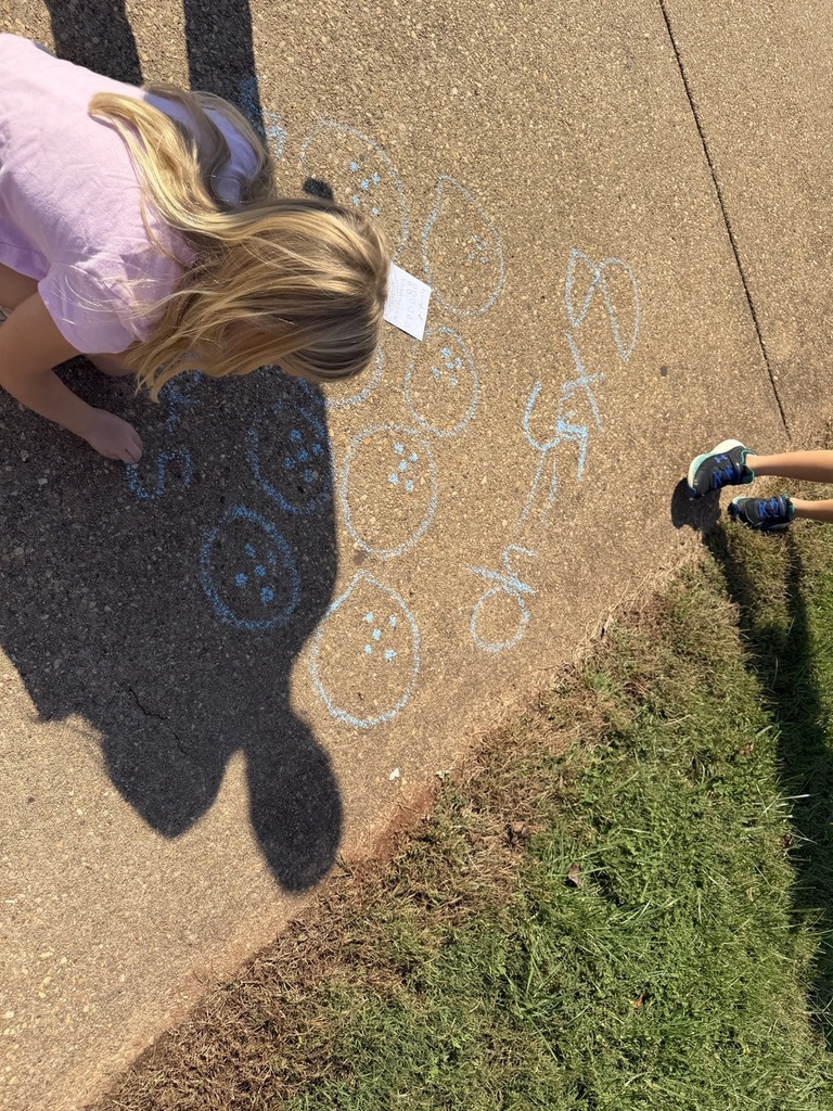 Child kneeling on concrete drawing circles, another child nearby. Shadows on the ground.