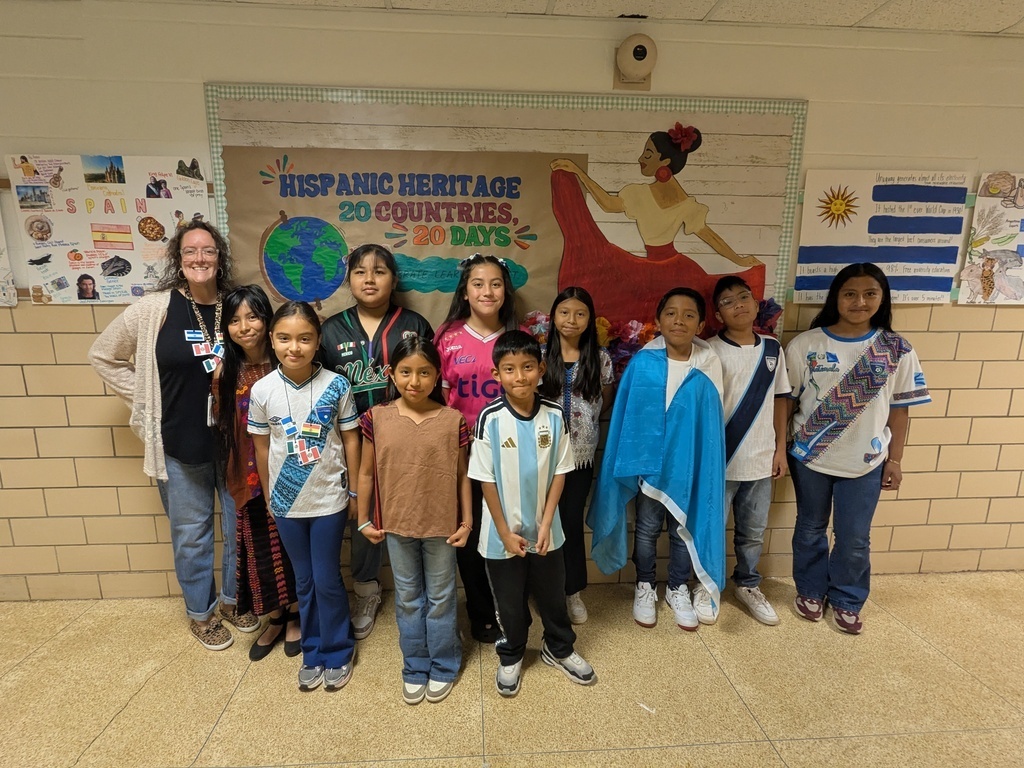 A group of students and adults pose for a photo in a classroom, with a Hispanic Heritage Month banner behind them.