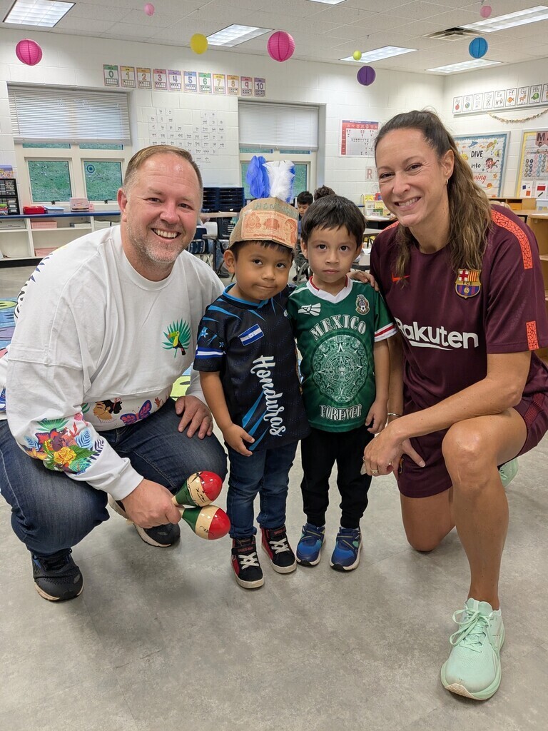 Three people, two adults and two children, in a classroom. One adult kneels, holding a toy.