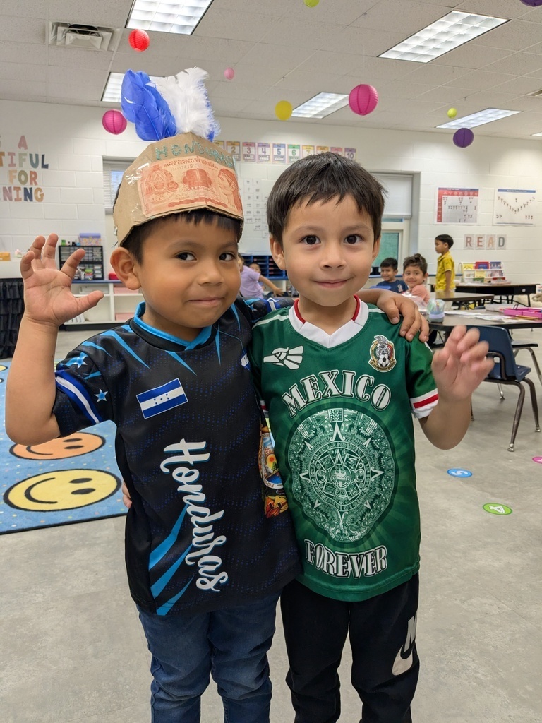 Two boys, one wearing a hat, pose for a photo. One wears a blue soccer jersey; the other wears a green one.