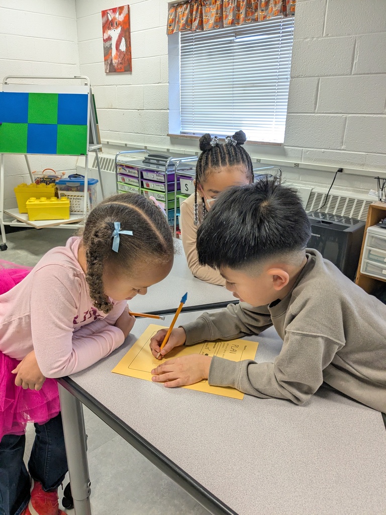 Children sitting at a desk in a classroom. A boy is writing on a yellow sheet of paper.