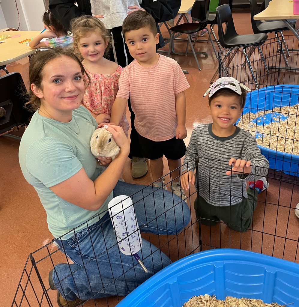 A woman kneels with two children and a rabbit in a cage. Another child stands nearby.