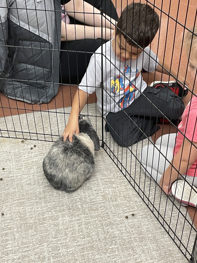 A woman kneels with two children and a rabbit in a cage. Another child stands nearby.