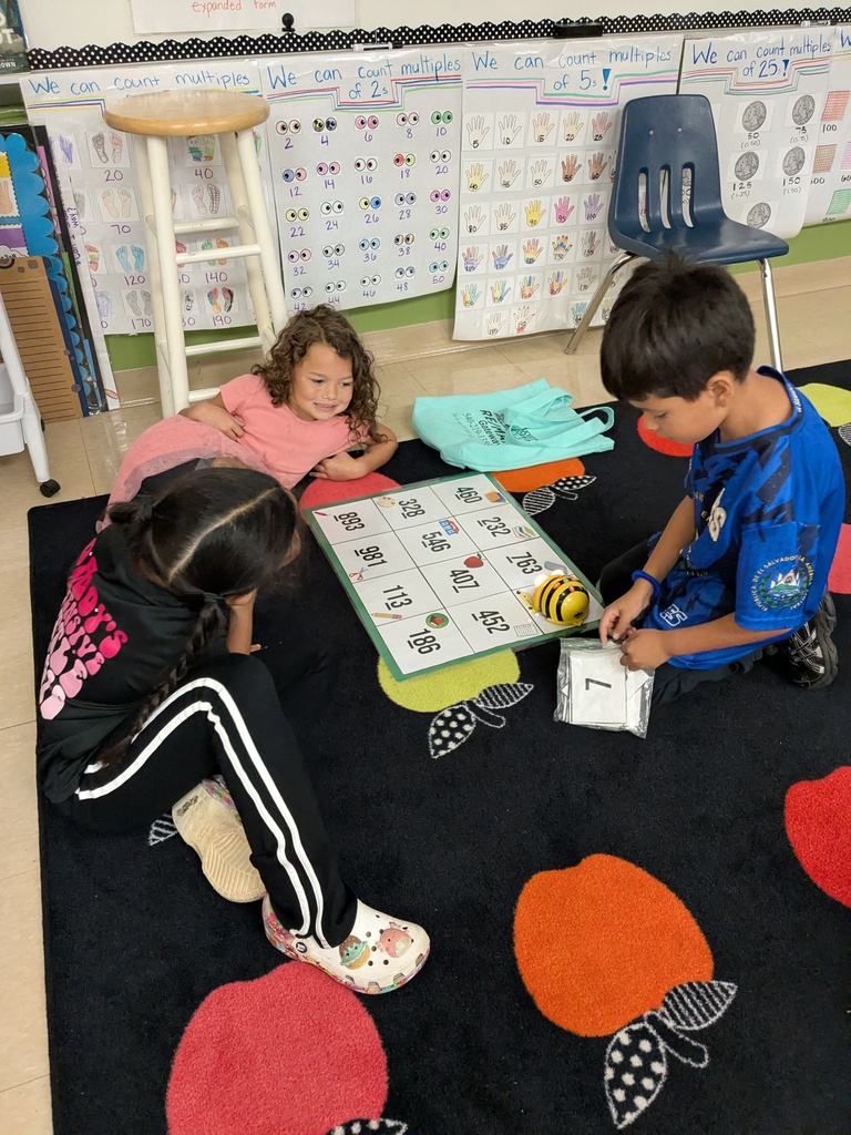 Three children on floor playing a game. One child uses a bee toy.