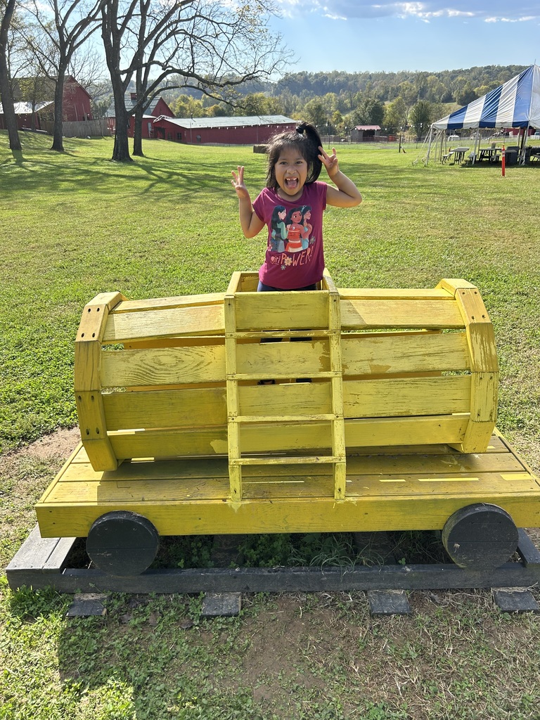 Child standing on top of a yellow toy train car in a grassy field.