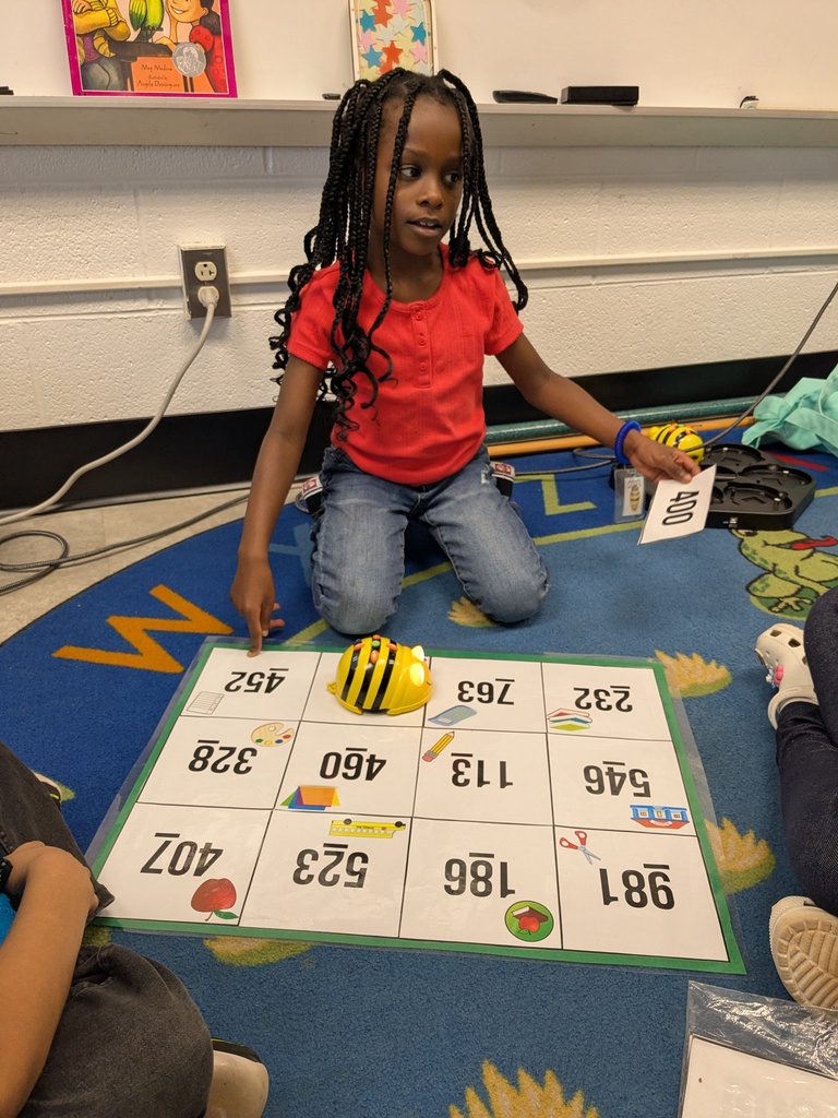 A young girl plays a word game with cards on a blue rug while others sit around.