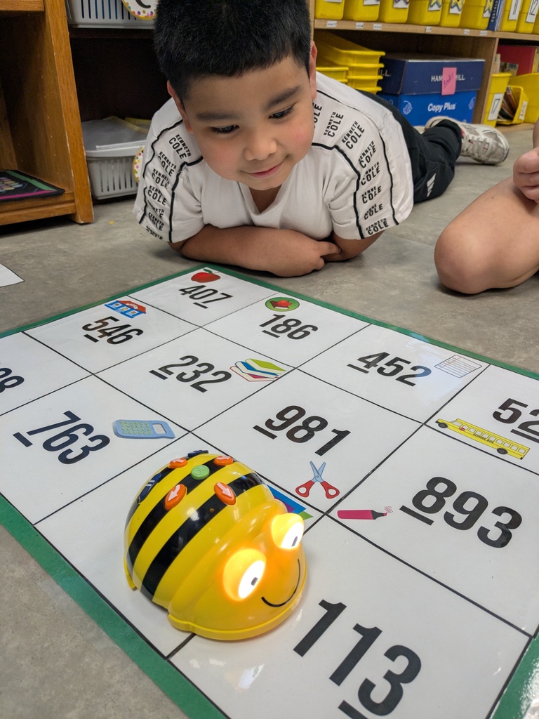 A young boy lying on a mat with a robot on a number grid in a classroom.