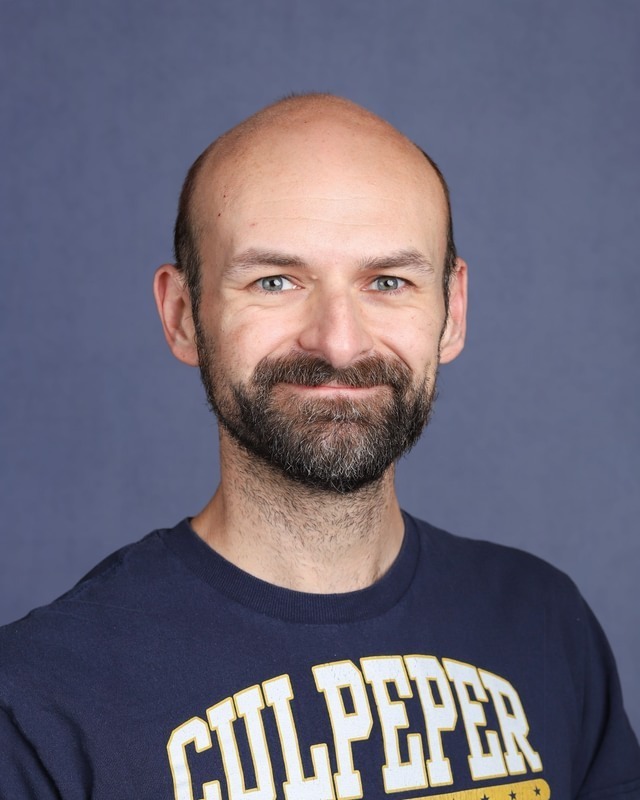 Man with beard and mustache smiles at camera. Wearing navy shirt with white "CULPEPER" text.