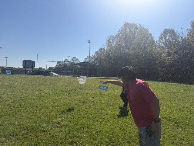Person with hand extended to catch frisbee, another person with frisbee behind, on sunny day.