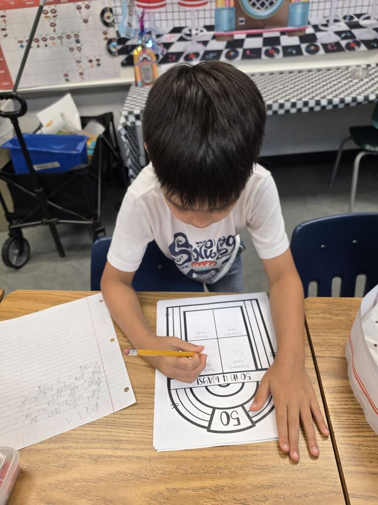 Child seated at a table, coloring in a basketball court outline, pencils and paper in front.