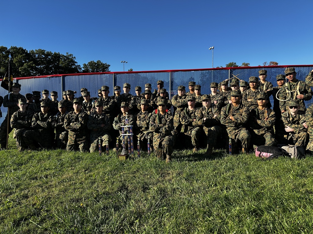 Many people in uniform posing for a photo, some kneeling and some standing, with a fence behind them.