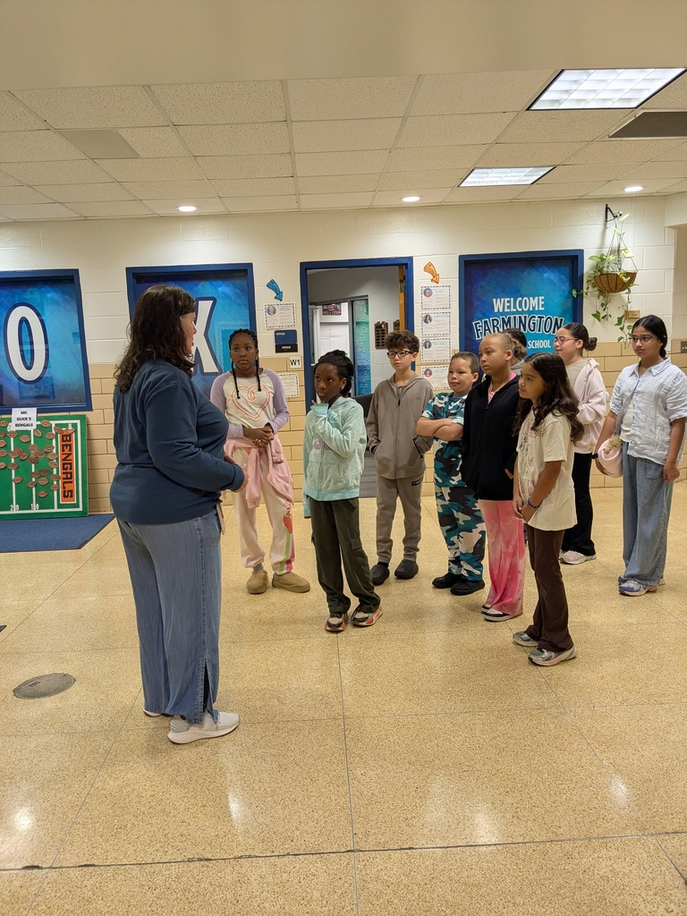 People stand in a hallway with numbered doors. Some wear sneakers and one person holds a microphone.