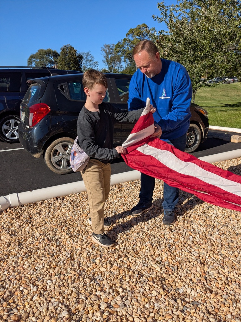 Adult and child hold American flag in parking lot. A car is in the background.