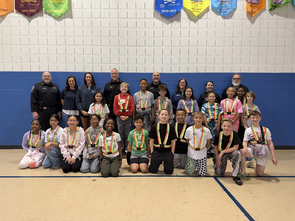 Group of students in medals poses for a photo in a gymnasium with blue walls.