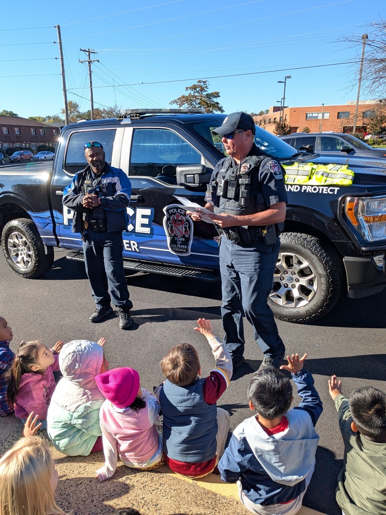 Two police officers standing in front of a pickup truck speak to children sitting on a curb.