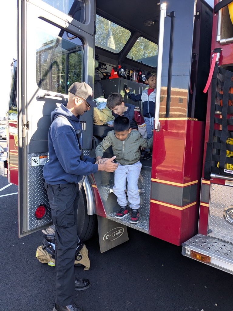 A man helps two children climb steps into a fire truck with its door open.