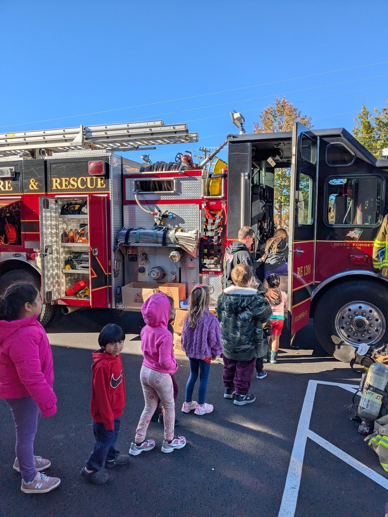 Children in jackets stand outside a red fire truck with a ladder on top.