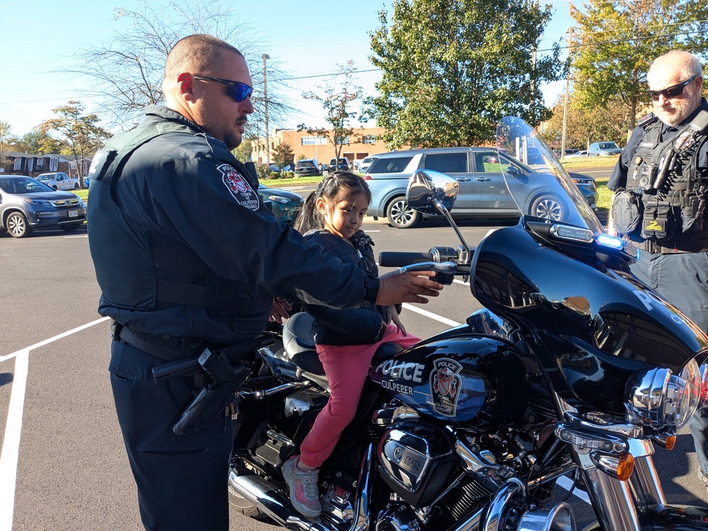 Two police officers in uniform help a young girl sit on the seat of a police motorcycle.