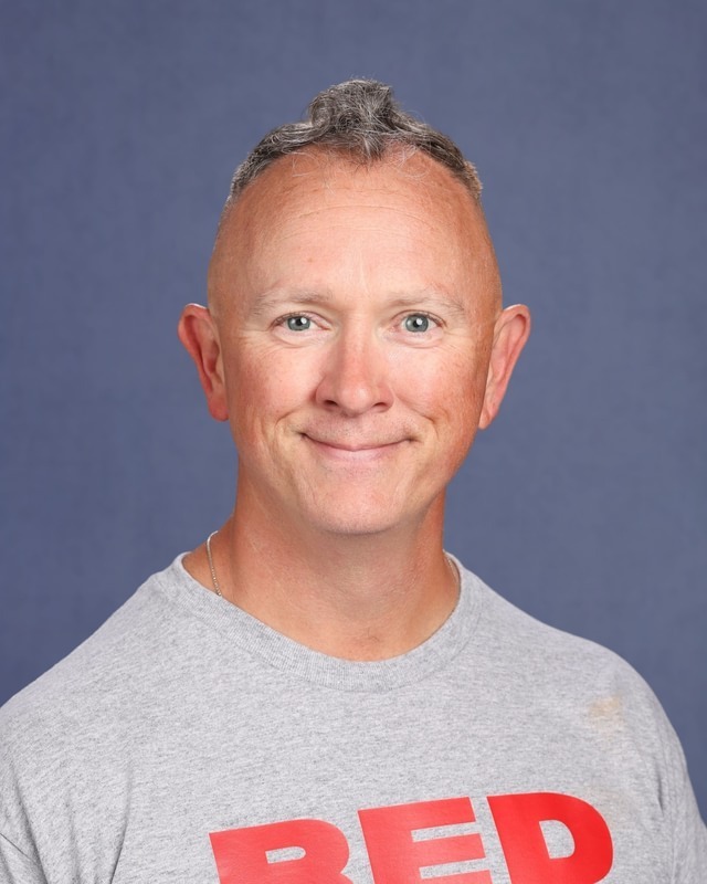 Man with short blond hair, smiling, wearing a gray shirt with red letters "REP" on the front.