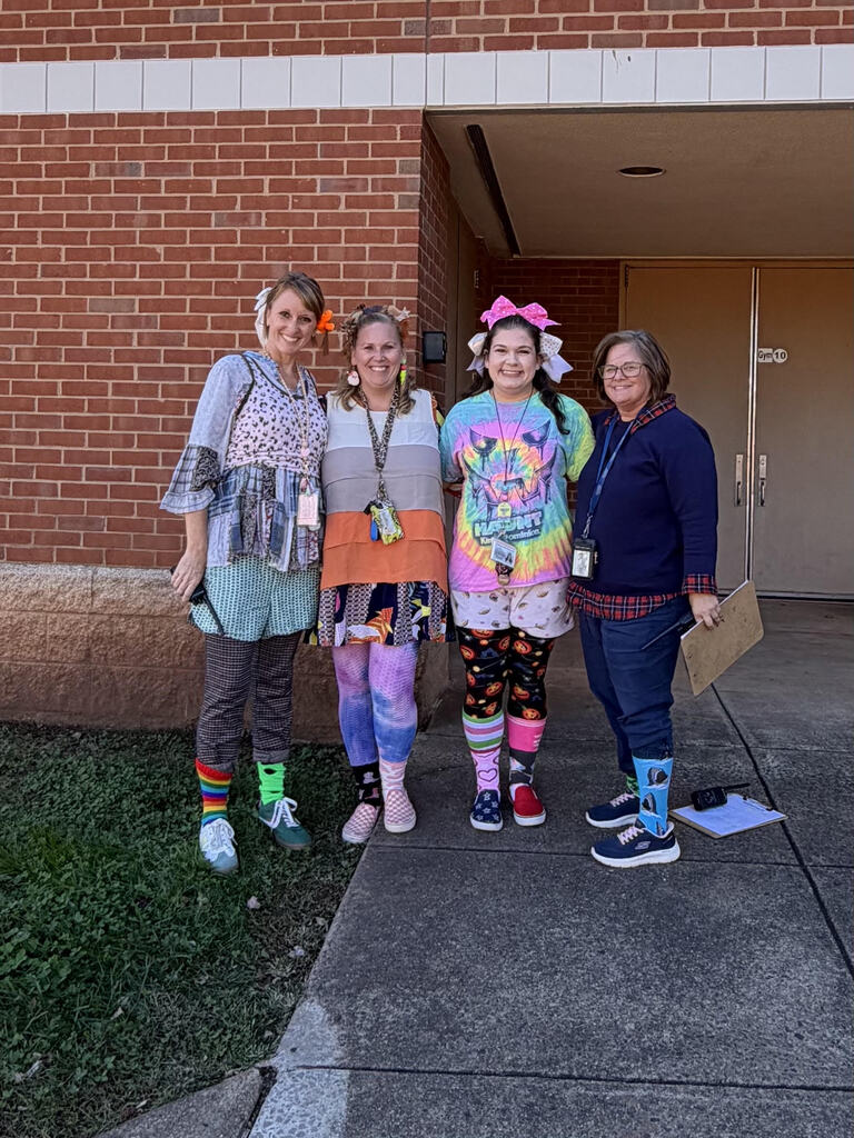 Five adults standing on a sidewalk. Two adults in front wear colorful socks and leggings. Two adults behind them wear IDs.