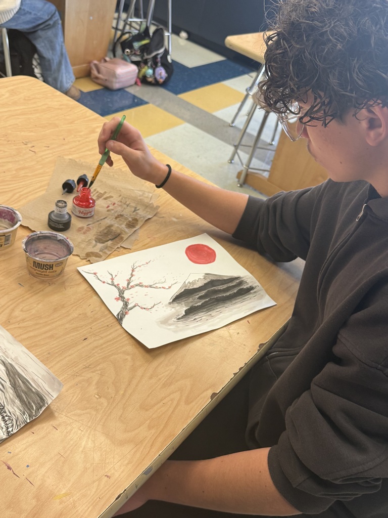 A student sitting at a table painting a landscape with ink and a brush.