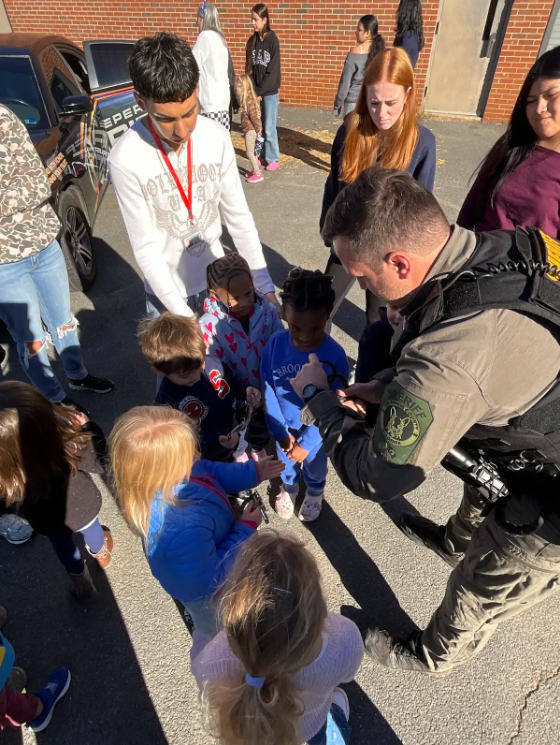 Police officer showing children handcuffs; children are standing in a circle around him, some wearing pajamas.