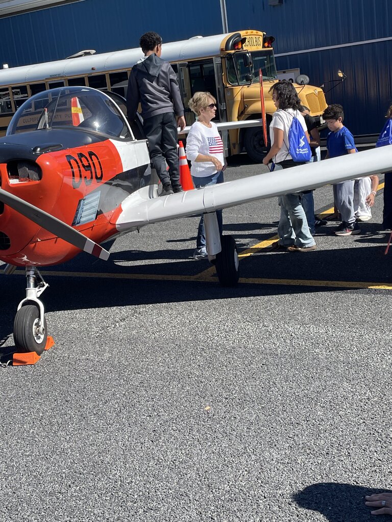 A small red and white plane parked on the tarmac, with people standing around it. One person stands on the wing.