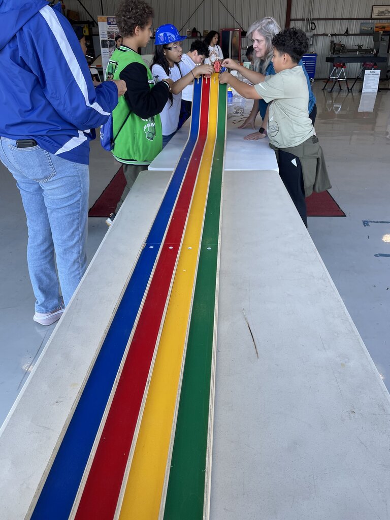 Several people working on a large wooden board with a rainbow pattern of colored stripes.