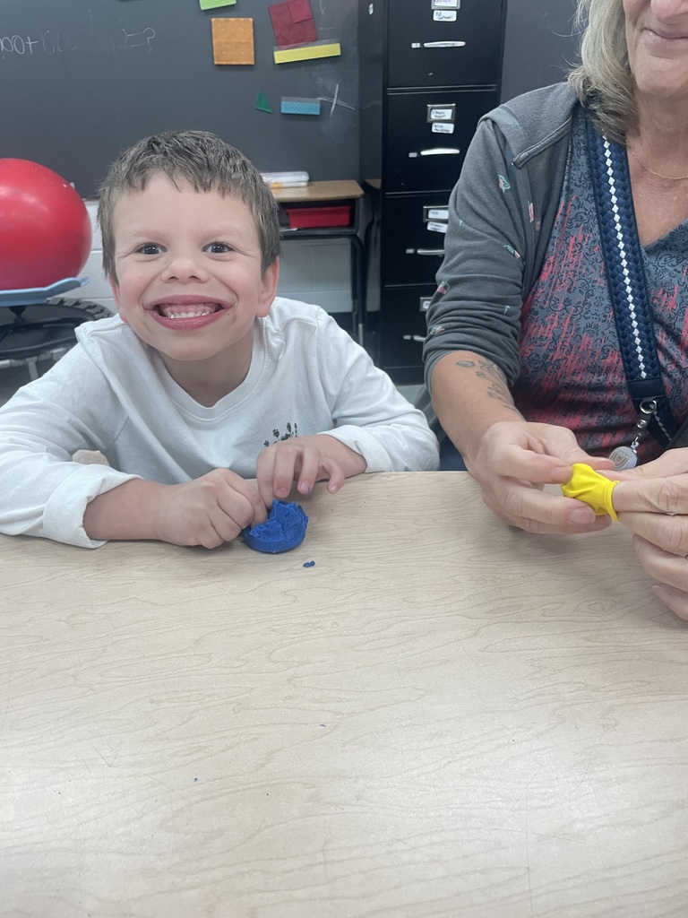 Child smiling, sitting at table holding blue object, next to adult holding yellow object.