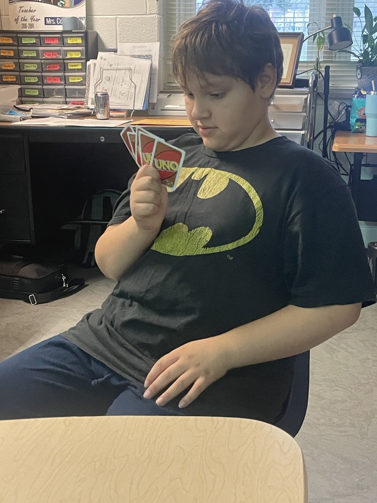 A boy sits at a desk with cards in hand, looking down at them.