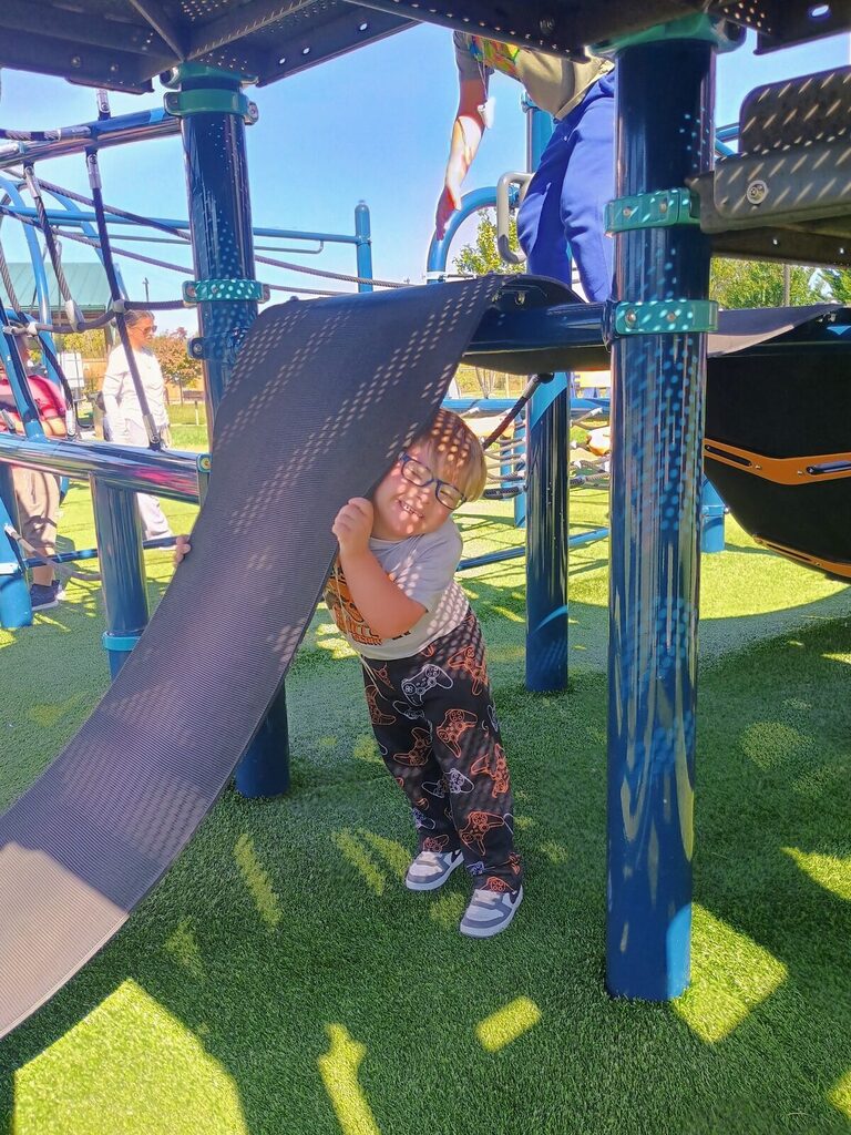 A young child holds onto a slide while standing on the ground, wearing a pair of glasses.