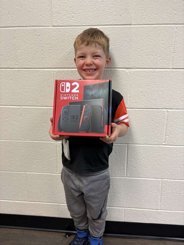 Child holding game console box with controller, smiling against a white wall with black border.