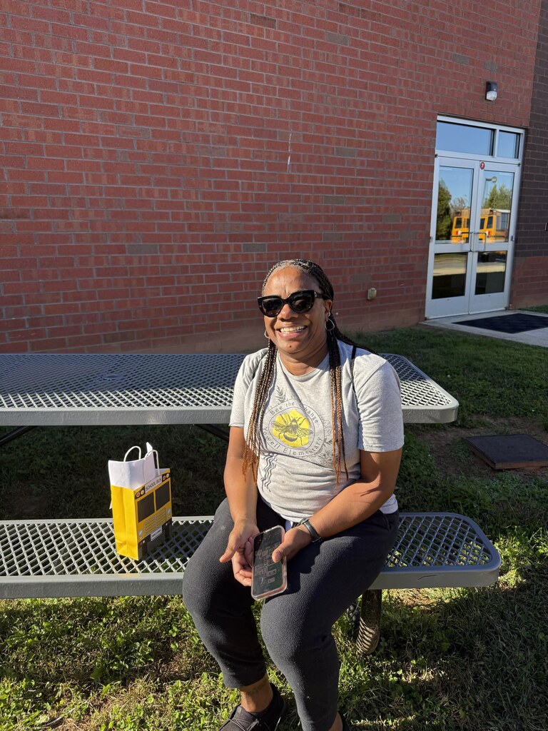 A person sits on a bench in front of a brick building, holding a cellphone.