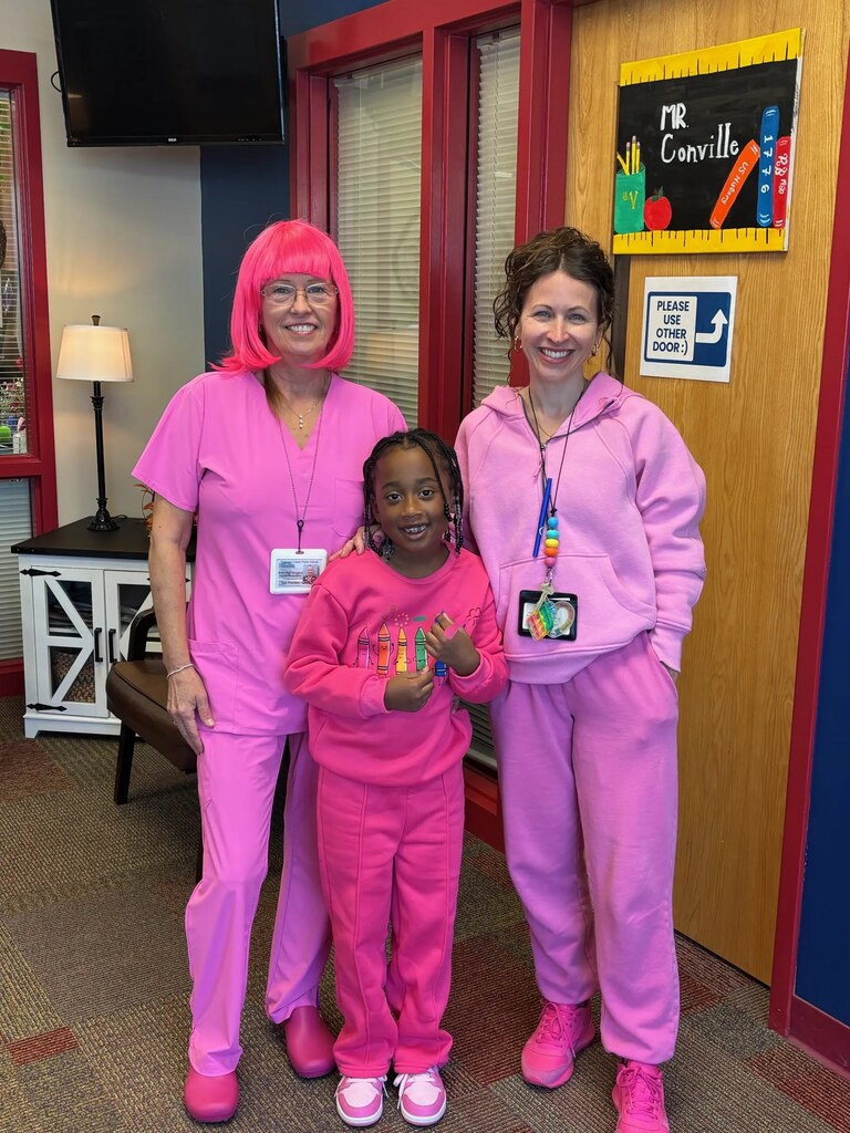 Three people in pink uniforms pose for a photo in a room with a door.