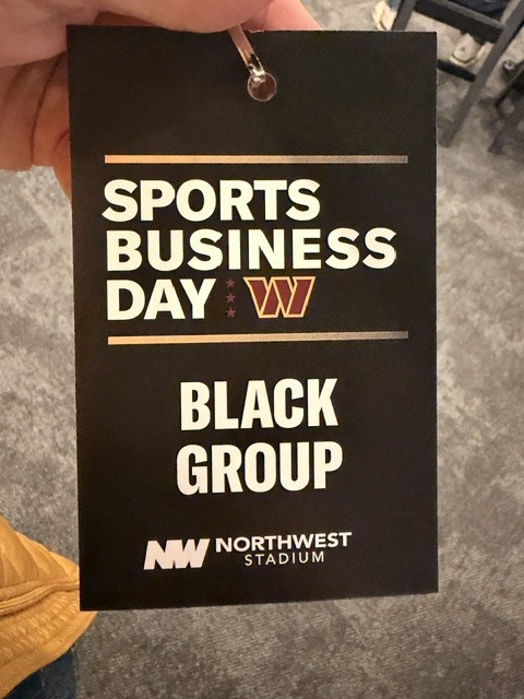 Black sign with white text "SPORTS BUSINESS DAY" and "BLACK GROUP" in center, with "NW NORTHWEST STADIUM" in lower left corner.