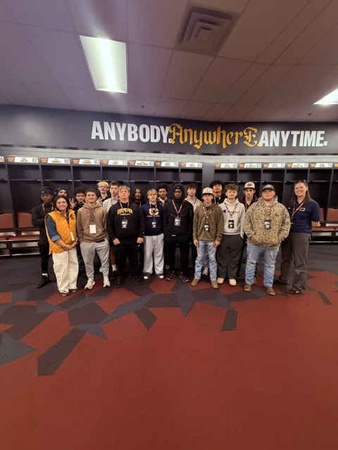 A group of people in hats and jackets pose for a photo in a locker room.