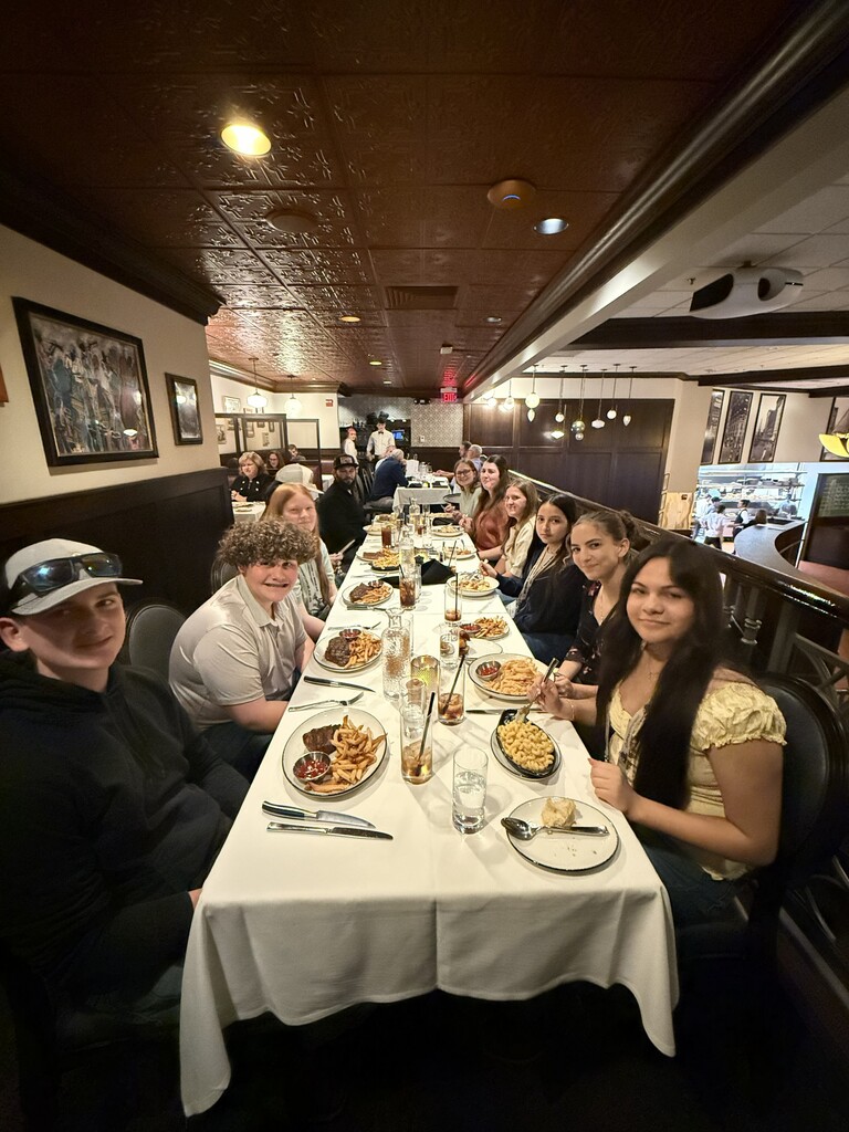 Group of people seated at long table with plates of food, drinks, and utensils in a restaurant.