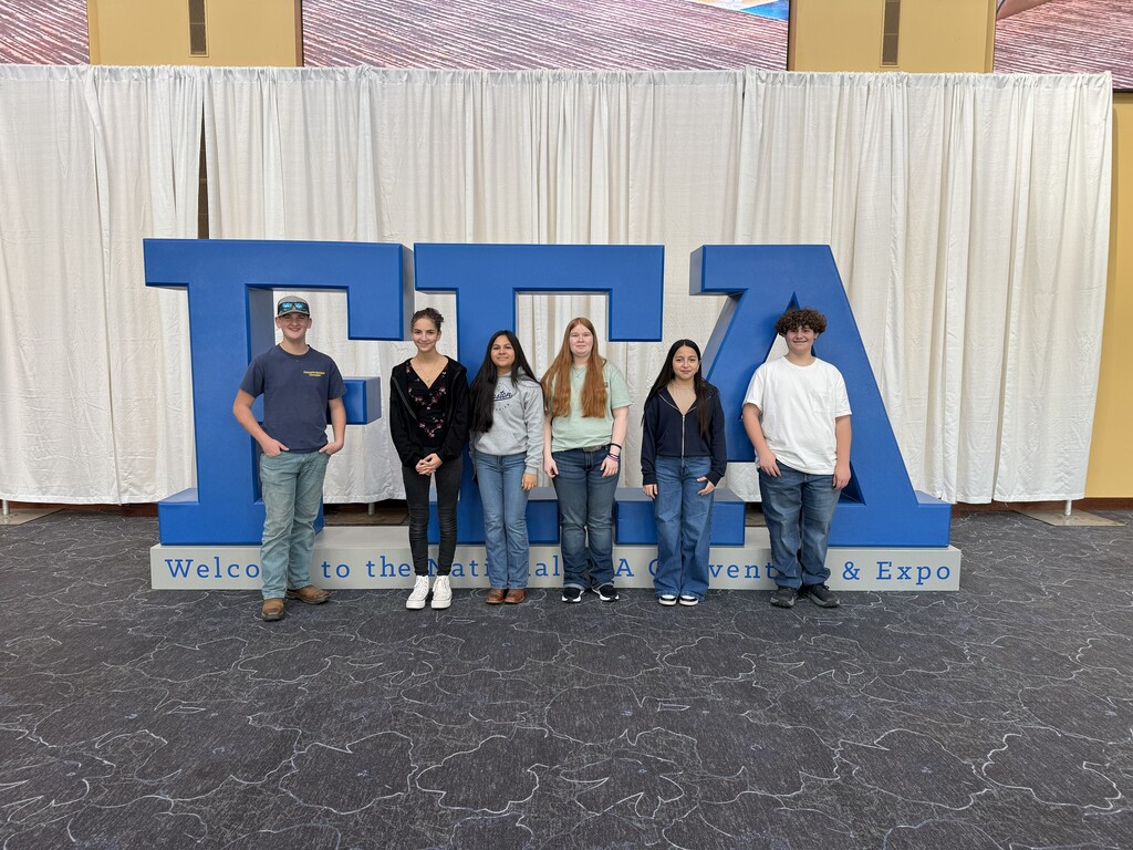Six students pose in front of a large blue sign with the letters FFA.