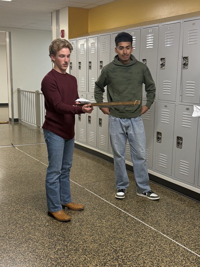 Two students standing next to lockers, each holding an object and looking at the camera.