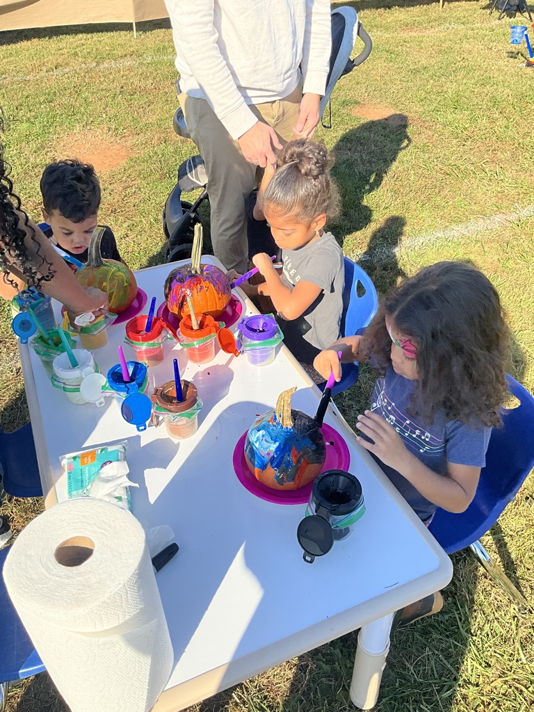 Children sit at a table with paper plates, paint, brushes, and other art supplies.
