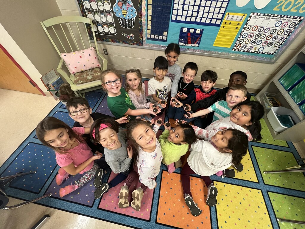 Group of children sitting in a circle on a colorful rug in a classroom.