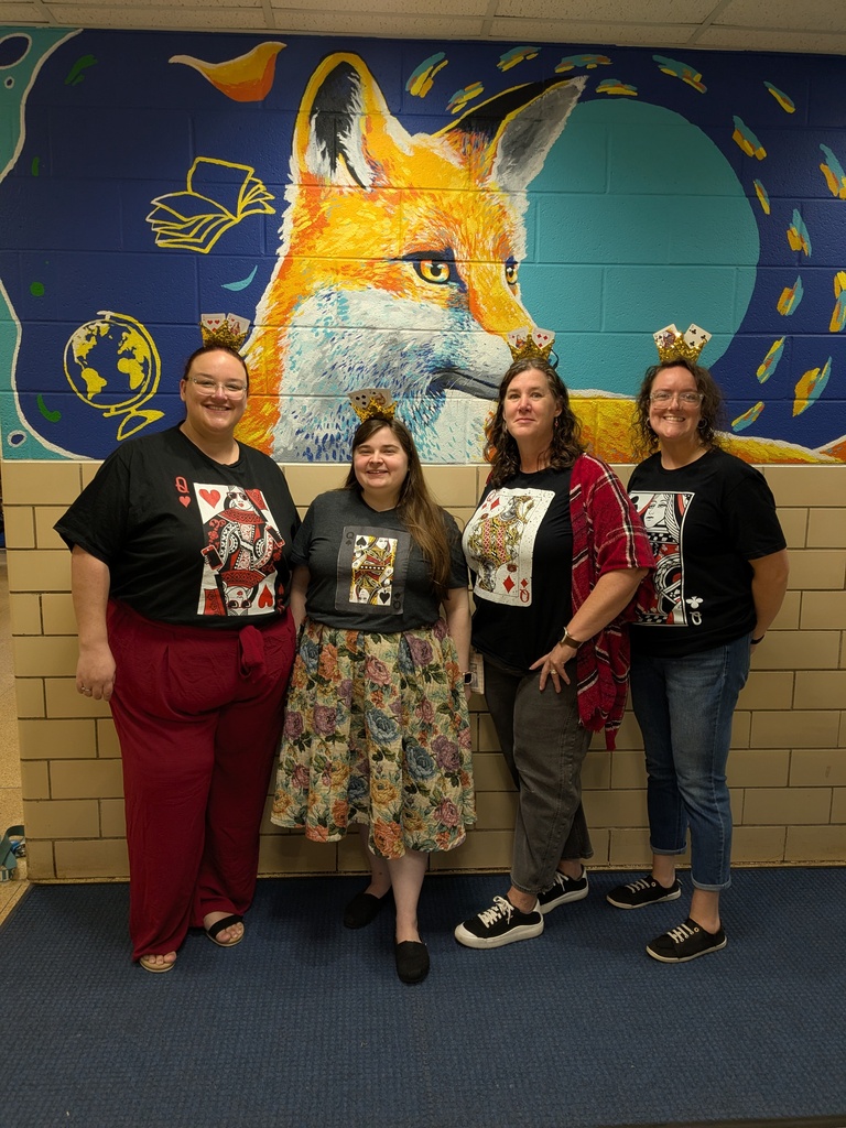 Four women stand in a hallway with a mural of a fox and books behind them.