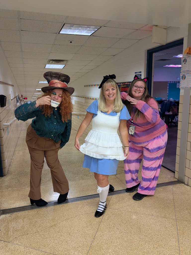 Three people in costume pose in a hallway with one drinking from a small cup.