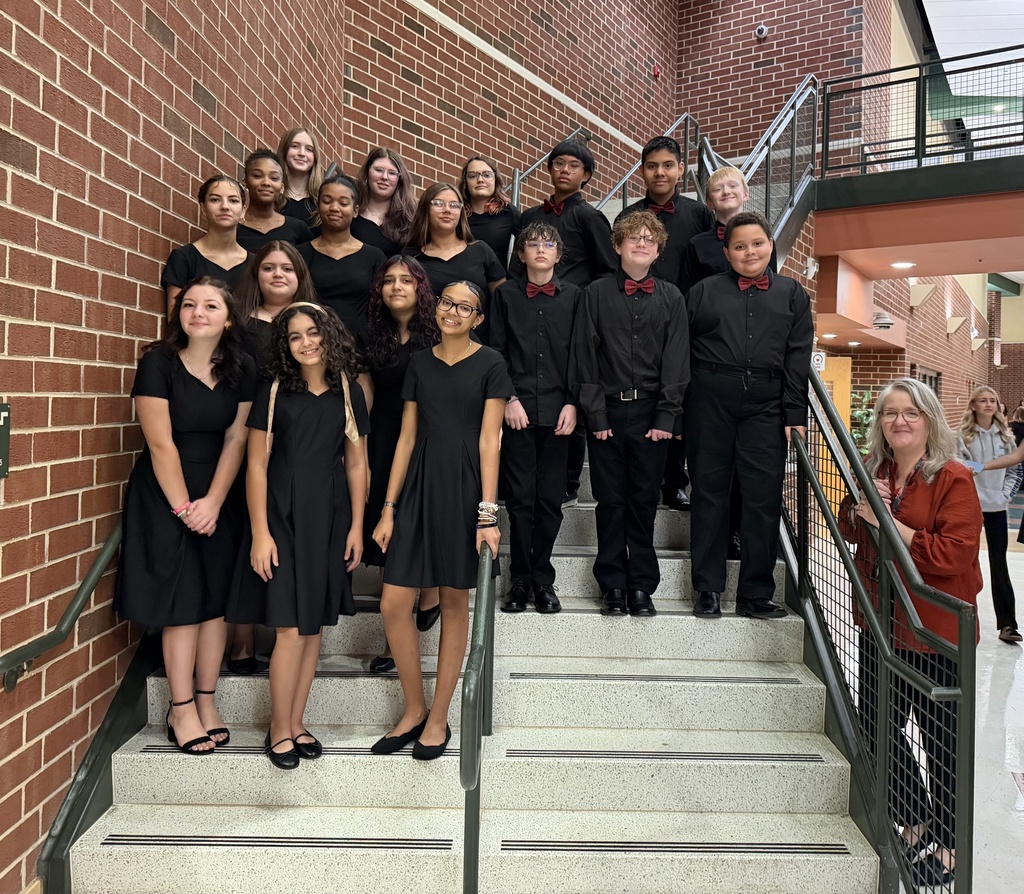 A group of students in black dresses and suits stand on concrete stairs, looking at the camera.
