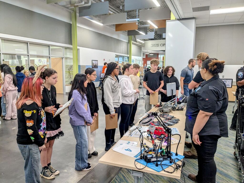 Group of students and adults standing around a table with electronics, wires, and a red robot