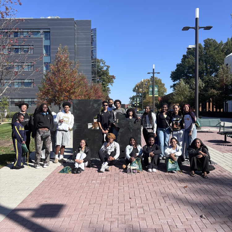 Group of students in casual clothing posing for a photo on a brick sidewalk.