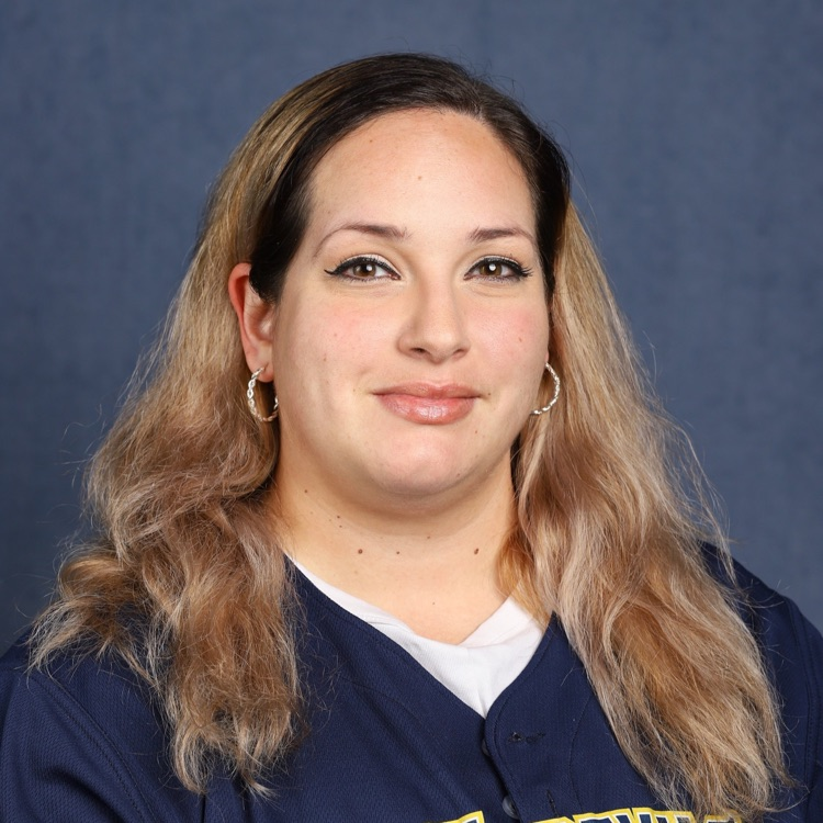 Woman with long hair wearing navy blue top with white undershirt and smiling at camera.