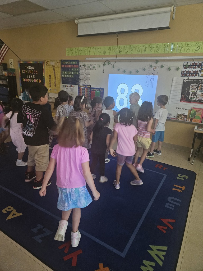 a class of kindergartners face the board and dance along to a song that counts from 1-100